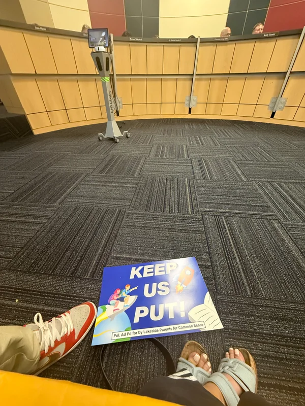 A Keep Us Put rally sign in the front row of the PfISD board room.